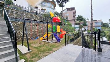 Un parque infantil con un tobogán y estructuras para escalar, rodeado de muros de piedra y edificios residenciales.