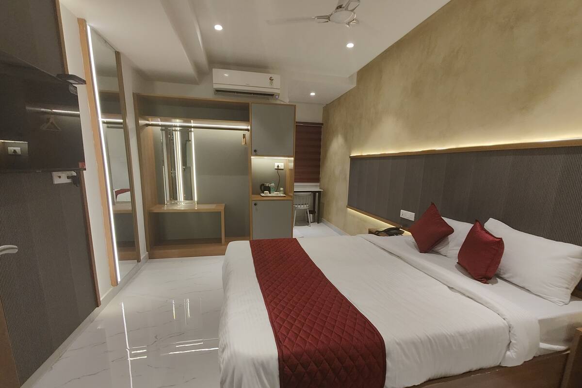 Una habitación de hotel moderna con una cama grande, un tocador con espejo, un escritorio pequeño y un equipo de aire acondicionado en la pared.