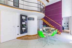 A modern interior with a curved staircase, a dining area with green chairs, and a purple accent wall.