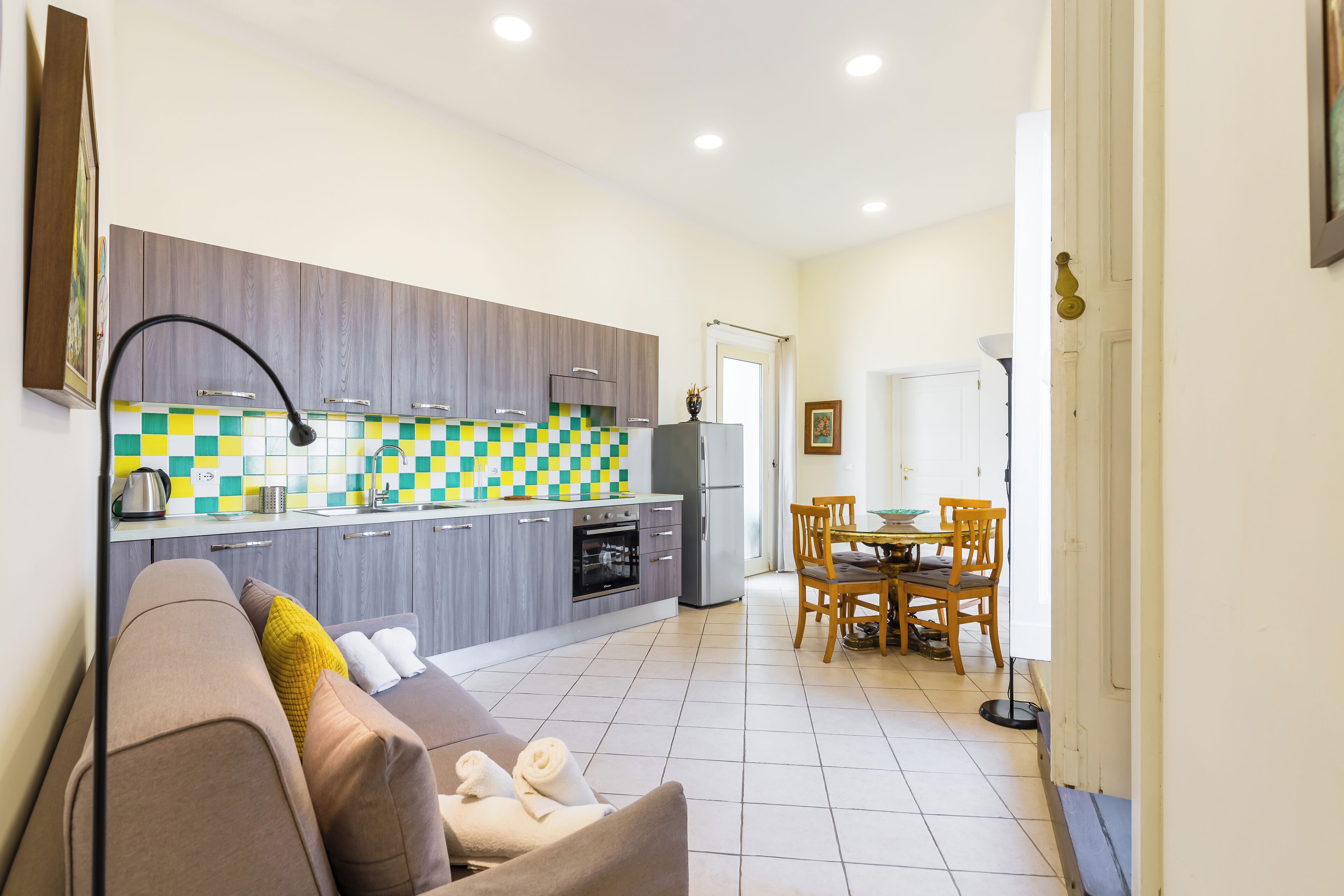 A modern kitchen with grey cabinets, a checkered backsplash, and a dining area with a table and chairs.