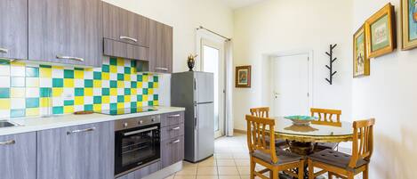 A modern kitchen with grey cabinets, a checkered backsplash, and a dining area with a round table and wooden chairs.