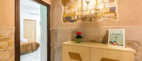 A hotel reception area with a stone wall, a bed in the background, and a sign on the counter.