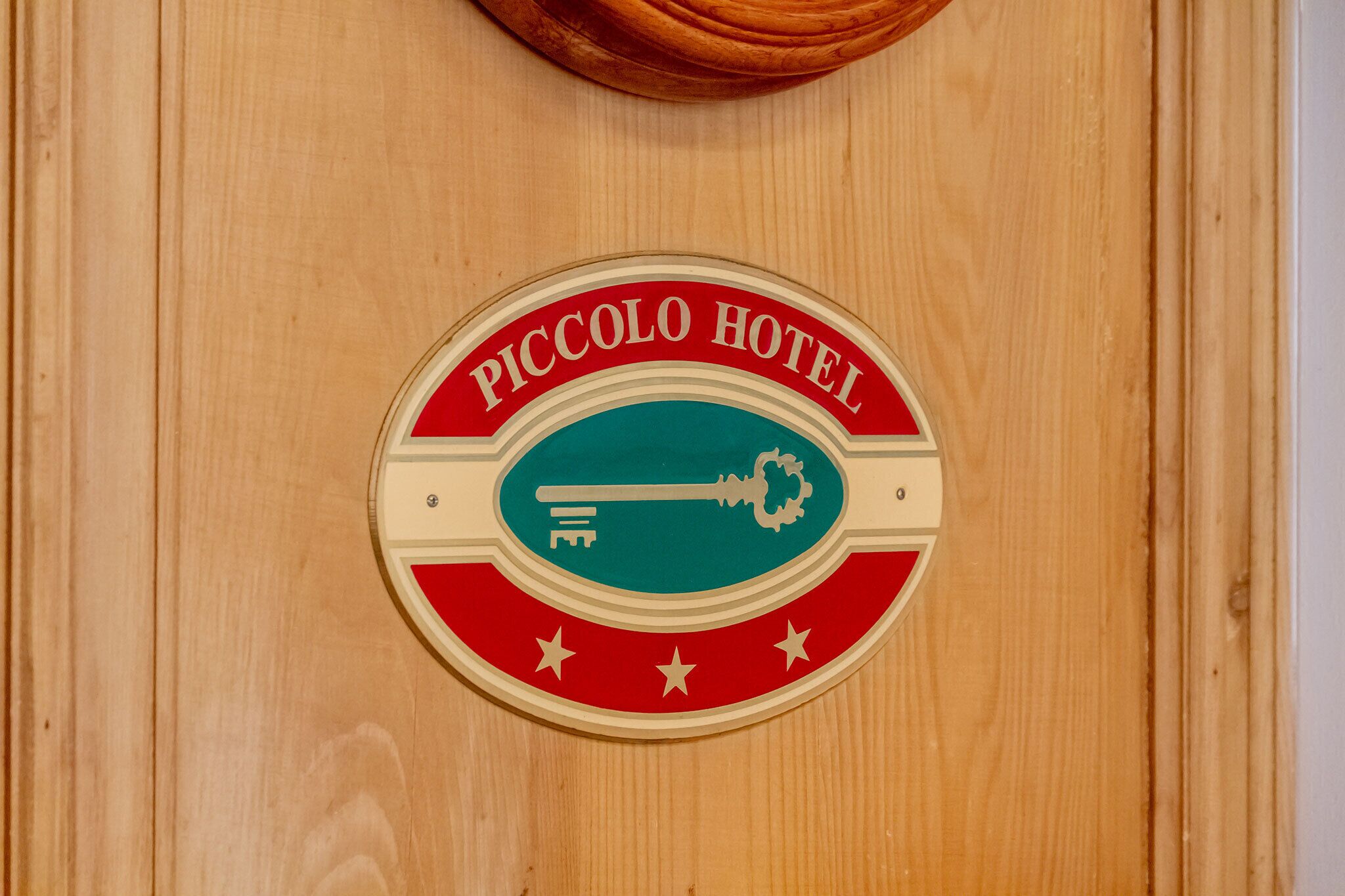Eine Holztür mit einem Schild, auf dem "PICCOLO HOTEL" steht und ein Schlüsselsymbol zeigt.