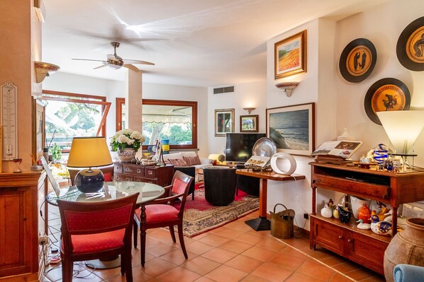 Un salon chaleureux comprenant un coin repas, un ventilateur de plafond, un téléviseur et divers objets décoratifs.