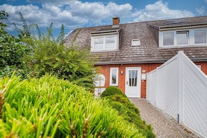 A two-story house with a brick facade, a white door, and a small window. - Ferienliebe Strandzeit - Cozy vacation apartment for up to 4 people in (Wenningstedt-Braderup (Sylt))