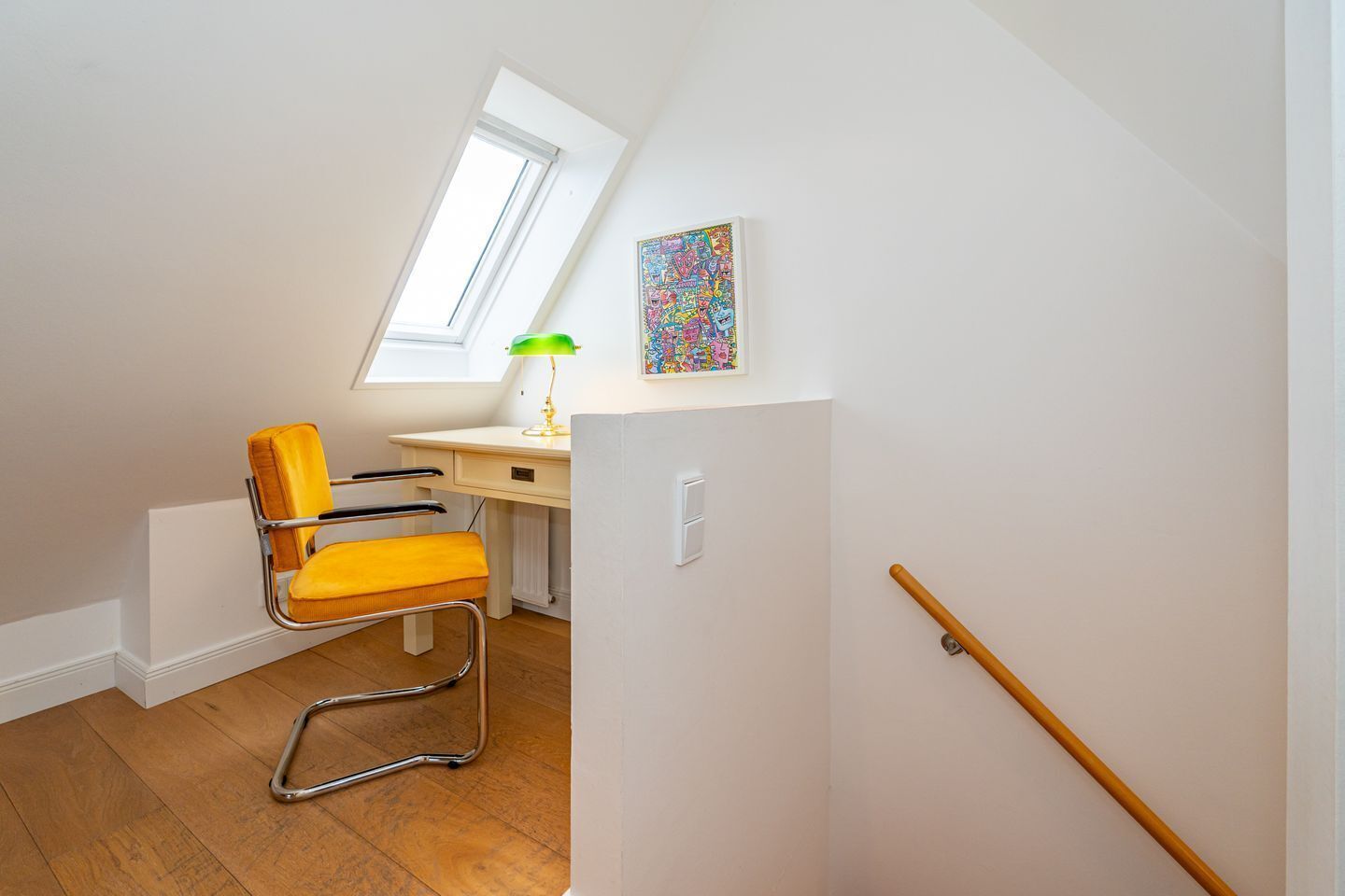 Een lichte, compacte kamer met een bureau, een stoel, een raam en kleurrijke kunst aan de muur.