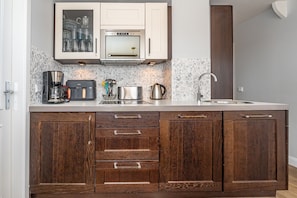 A kitchen with a built-in oven, microwave, and coffee maker. There are cabinets with wooden handles and a backsplash with a mosaic tile design. - Ferienliebe Strandzeit - Cozy vacation apartment for up to 4 people in (Wenningstedt-Braderup (Sylt))