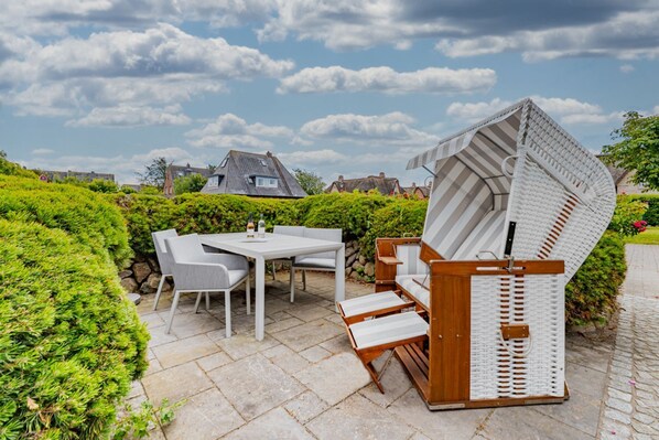 Une terrasse extérieure avec une table et des chaises blanches, un banc en bois et une structure blanche incurvée.