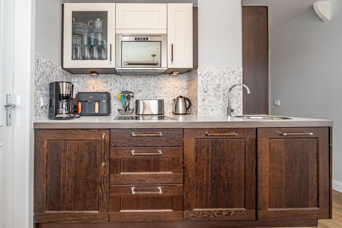 A kitchen with a built-in oven, microwave, and coffee maker. There are cabinets with wooden handles and a backsplash with a mosaic tile design.