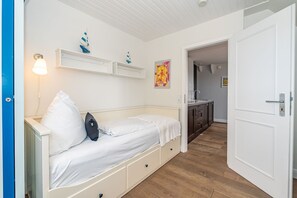 Een knus slaapkamer met een bed, nachtkastjes en een klein plankje met decoratieve spullen. Een gang leidt naar een badkamer en een keukenhoek.