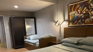 A modern bedroom with a large bed, a smaller bed, a wardrobe, a mirror, and a painting on the wall.