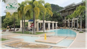 A swimming pool area with a lifeguard chair, palm trees, and a building with a modern design.