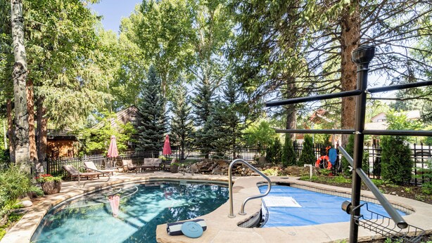 A swimming pool with a stone deck, surrounded by trees and a fence.