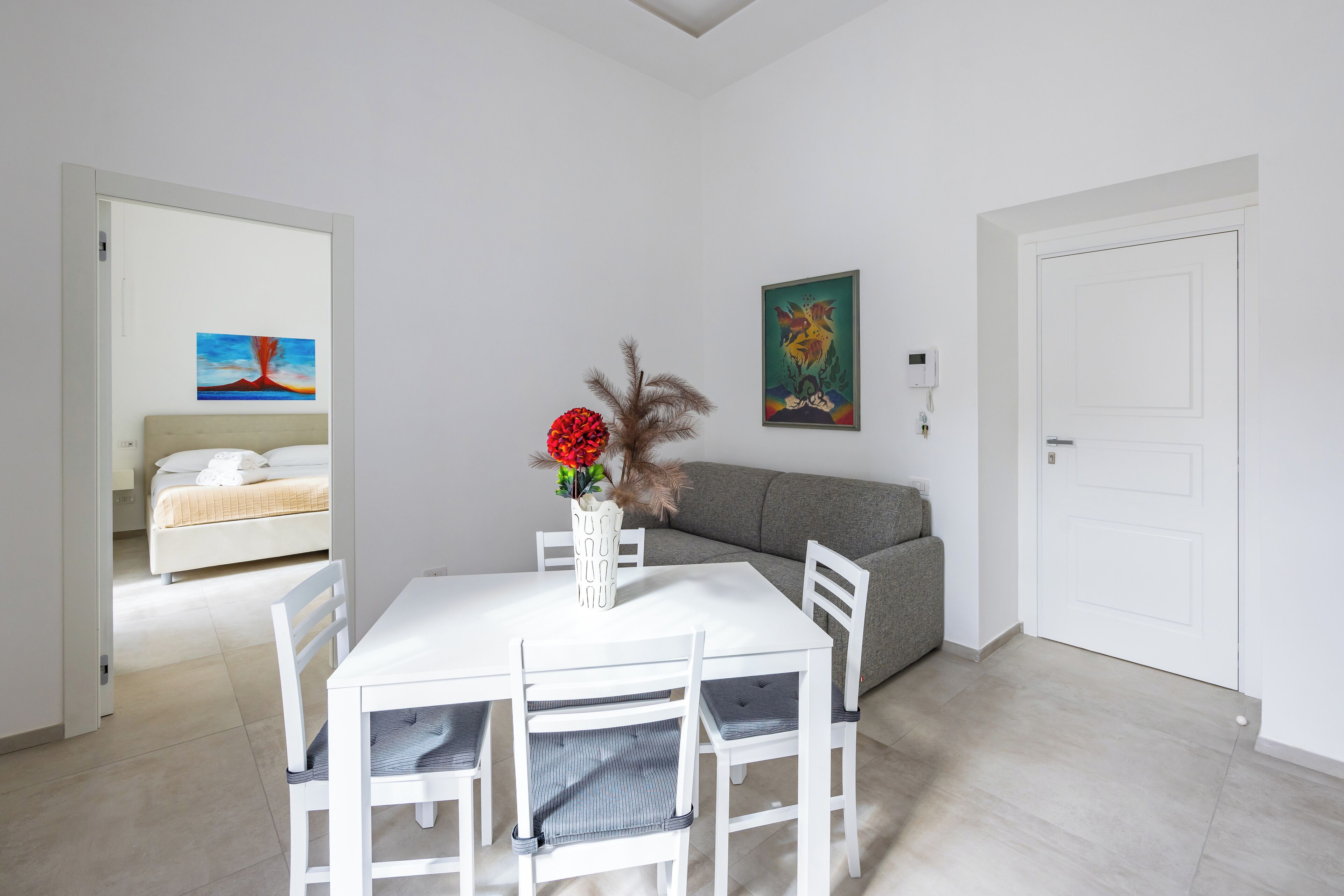 Ein modernes Wohnzimmer mit einem weißen Esstisch, vier Stühlen, einem grauen Sofa und einer weißen Tür.