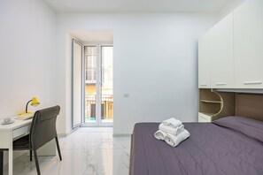 A modern hotel room with a desk, chair, bed, and a view of the outside balcony. - Marcellino Comfort House by Napoliapartments (Naples)