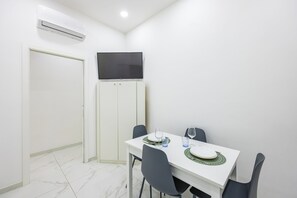 A dining area with a white table, black chairs, and a flat-screen TV mounted on the wall. - Marcellino Comfort House by Napoliapartments (Naples)