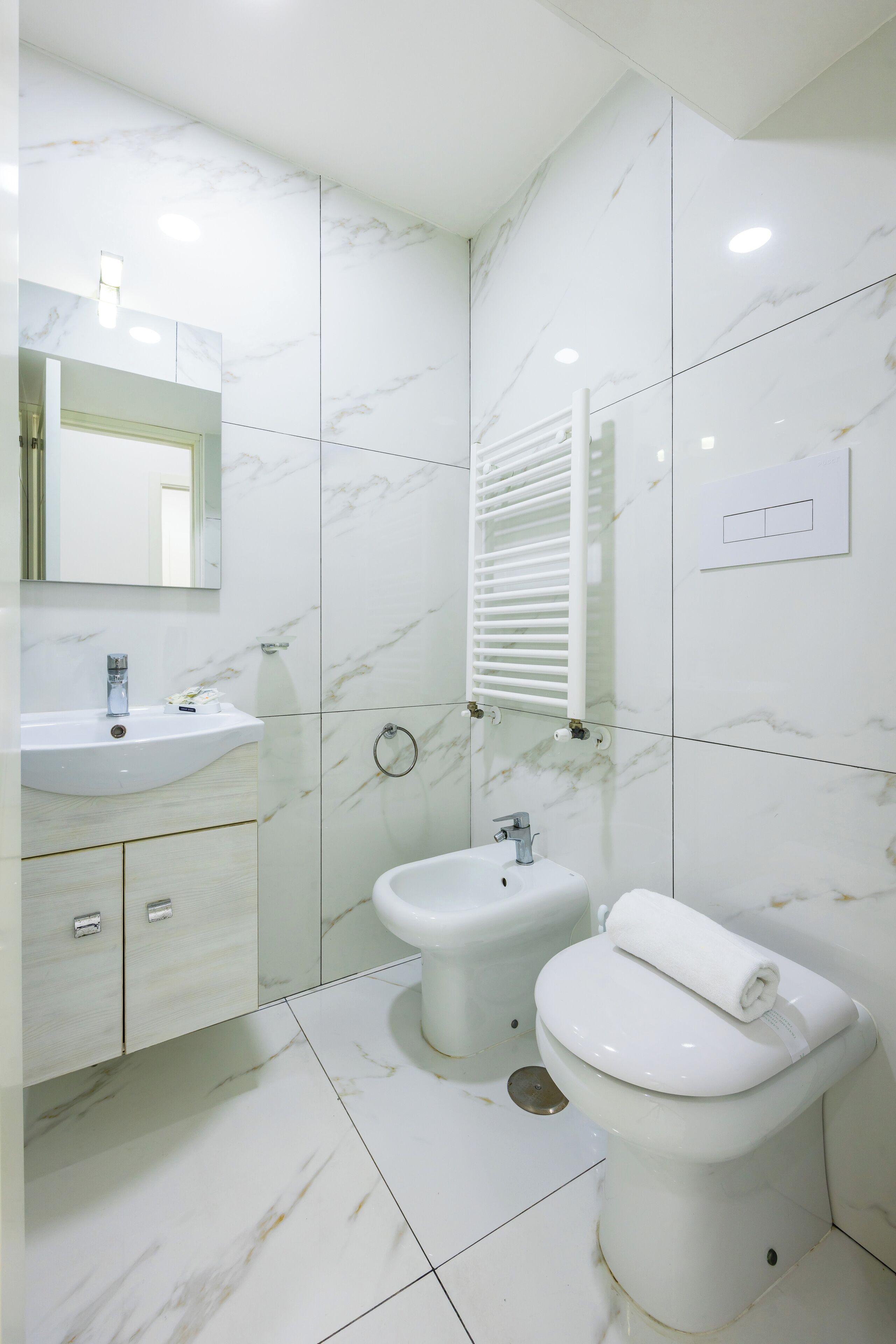 Een moderne badkamer met een wit wastafel, twee hygiëneschuiven, een toilet en een spiegel.