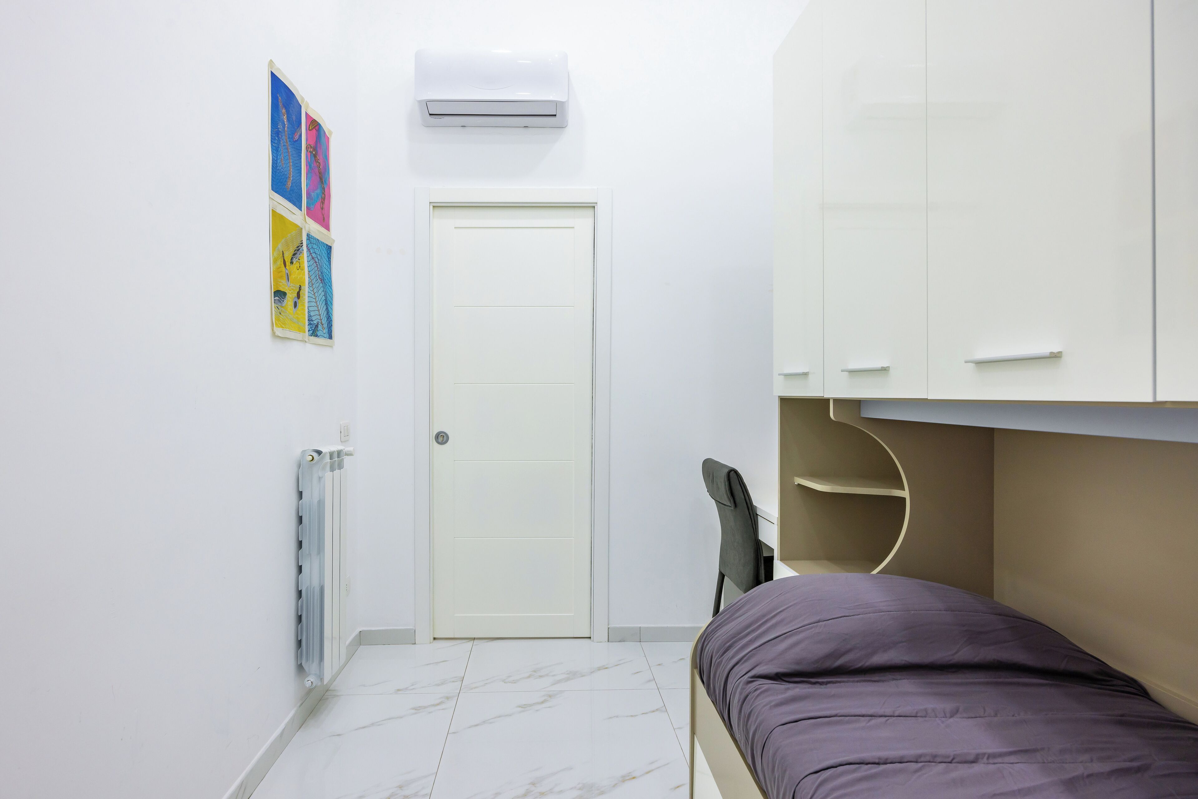 Une chambre à coucher avec un lit, un radiateur, une porte et un climatiseur fixé au mur.