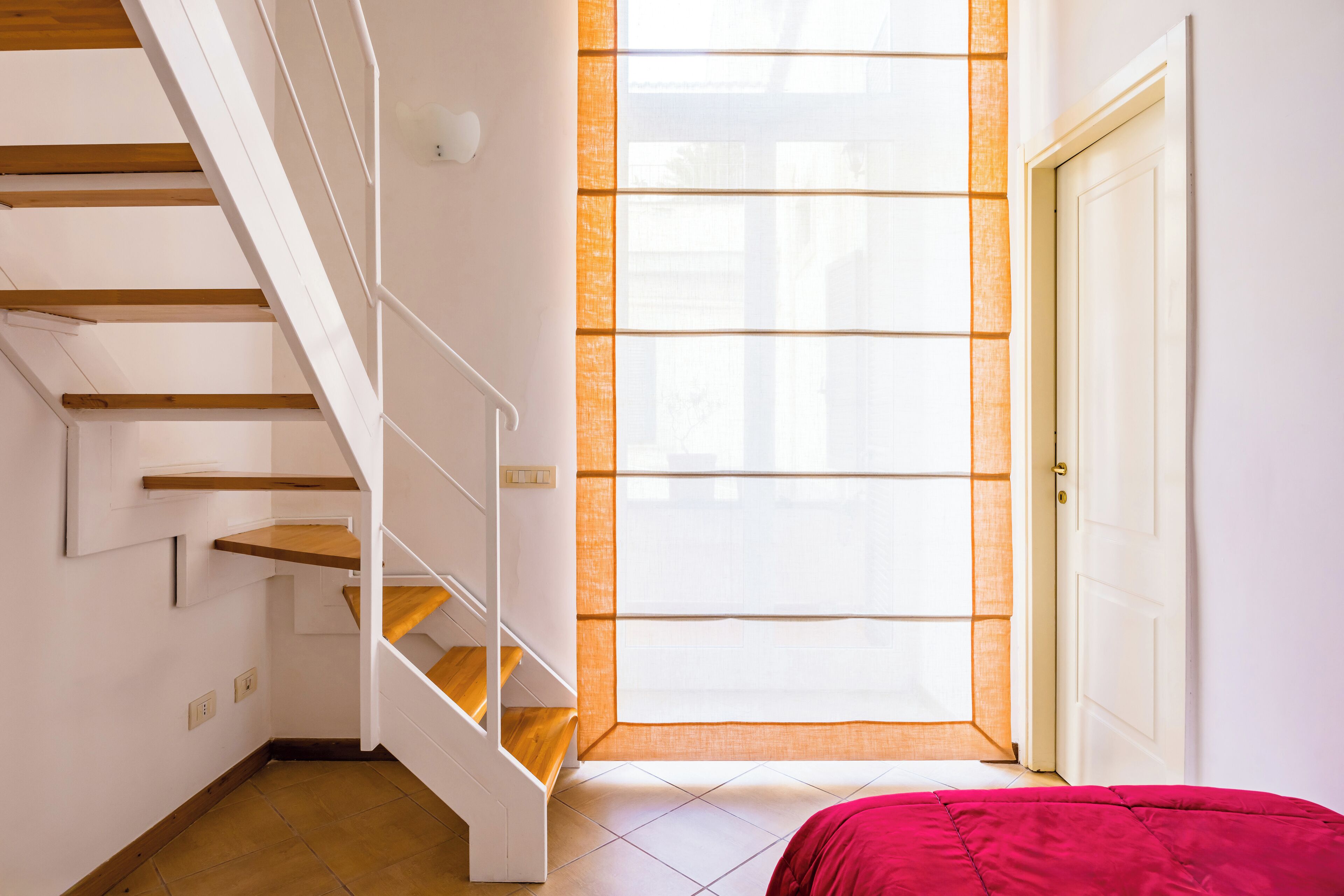 Um quarto com escada, janela com persianas e porta.