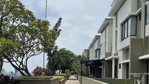A modern residential building with a paved walkway, greenery, and a clear sky.
