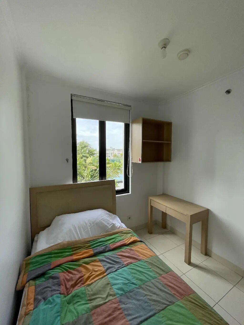 A bedroom with a bed, a window, a desk, and a shelf.