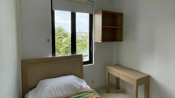 A bedroom with a bed, a window, a desk, and a shelf.