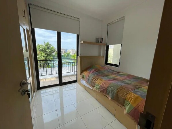 Un dormitorio con una cama, un puerta corrediza de vidrio a un balcón y una pequeña repisa sobre la cama.