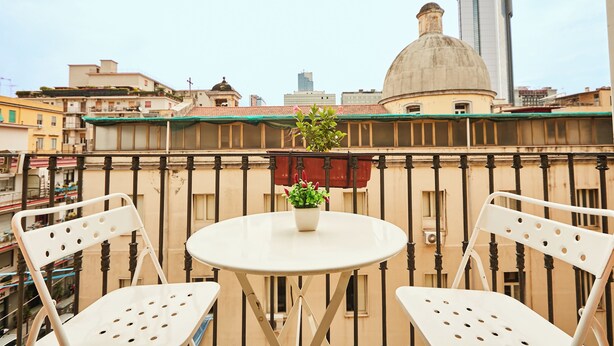 A balcony with two white chairs and a small table, a potted plant, and a view of city buildings. - Napoli Fuori (Naples)
