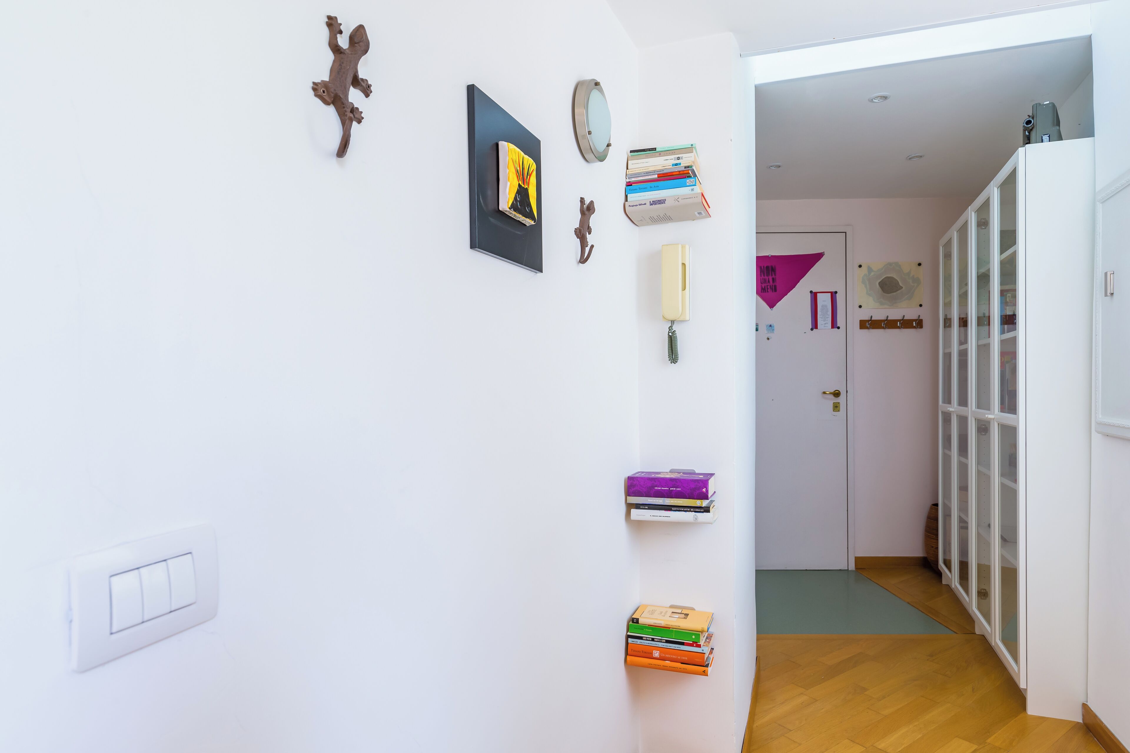 Un couloir avec un mur blanc, une porte dotée d’un panneau en verre et un plancher en bois.