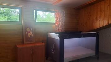Een kamer met houten wanden, een stapelbed, een klein kastje en twee ramen voorzien van gordijnen.