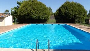 A rectangular swimming pool with clear blue water, surrounded by a brick deck and two trees. - 2-bedroom duplex with swimming pool and tennis court (Naujac-sur-Mer)
