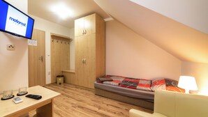 A small, well-lit room with a bed, a desk with a computer and remote controls, a wooden wardrobe, and a television displaying 'motorrest LUMIA'. - Motorest Lumík (Slovenske Darmoty)