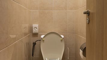 Un baño pequeño y moderno con inodoro, un cubo de basura y un secador de manos.