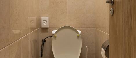 Un baño pequeño y moderno con inodoro, un cubo de basura y un secador de manos.