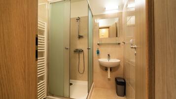 A modern bathroom with a glass-enclosed shower, a white sink, and a trash bin.