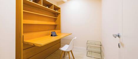 A small, well-lit room with a wooden desk, a white chair, and a glass shelf unit.