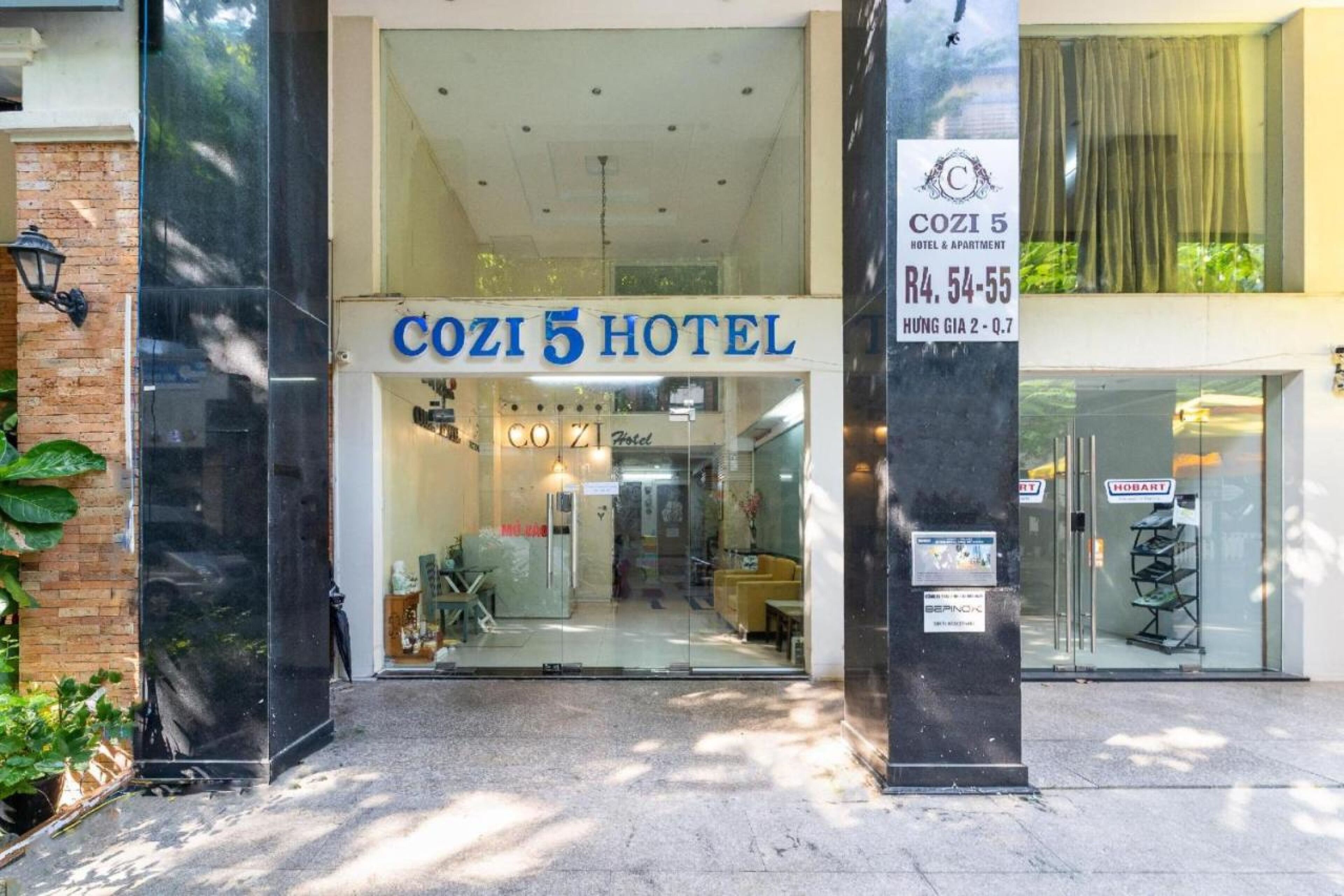 The exterior of Cozi 5 Hotel with a clear entrance, a visible reception area, and a sign indicating the hotel's name and address.
