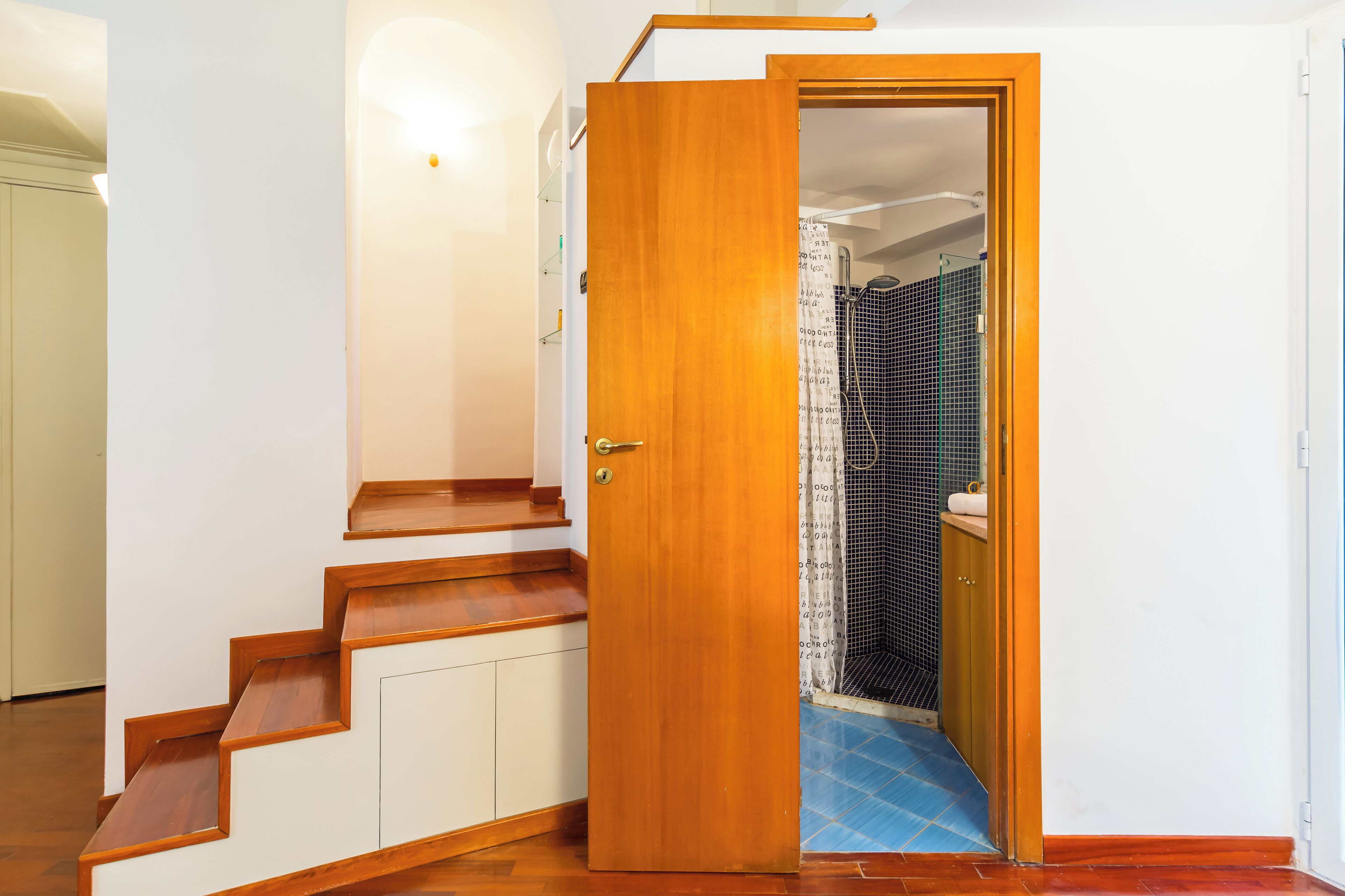 A wooden staircase leading to a bathroom with a shower area.