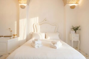 A hotel room with a large bed, a bedside table, a nightstand, and a wall-mounted light fixture. - Marchesa – Two-Bedroom Suite with Panoramic Terrace in the Historic Center (Monopoli)