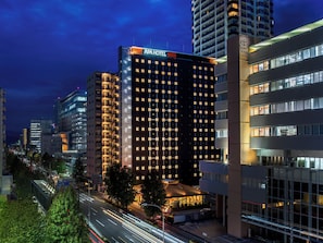 A multi-story hotel with a modern facade, illuminated windows, and a visible parking area.
