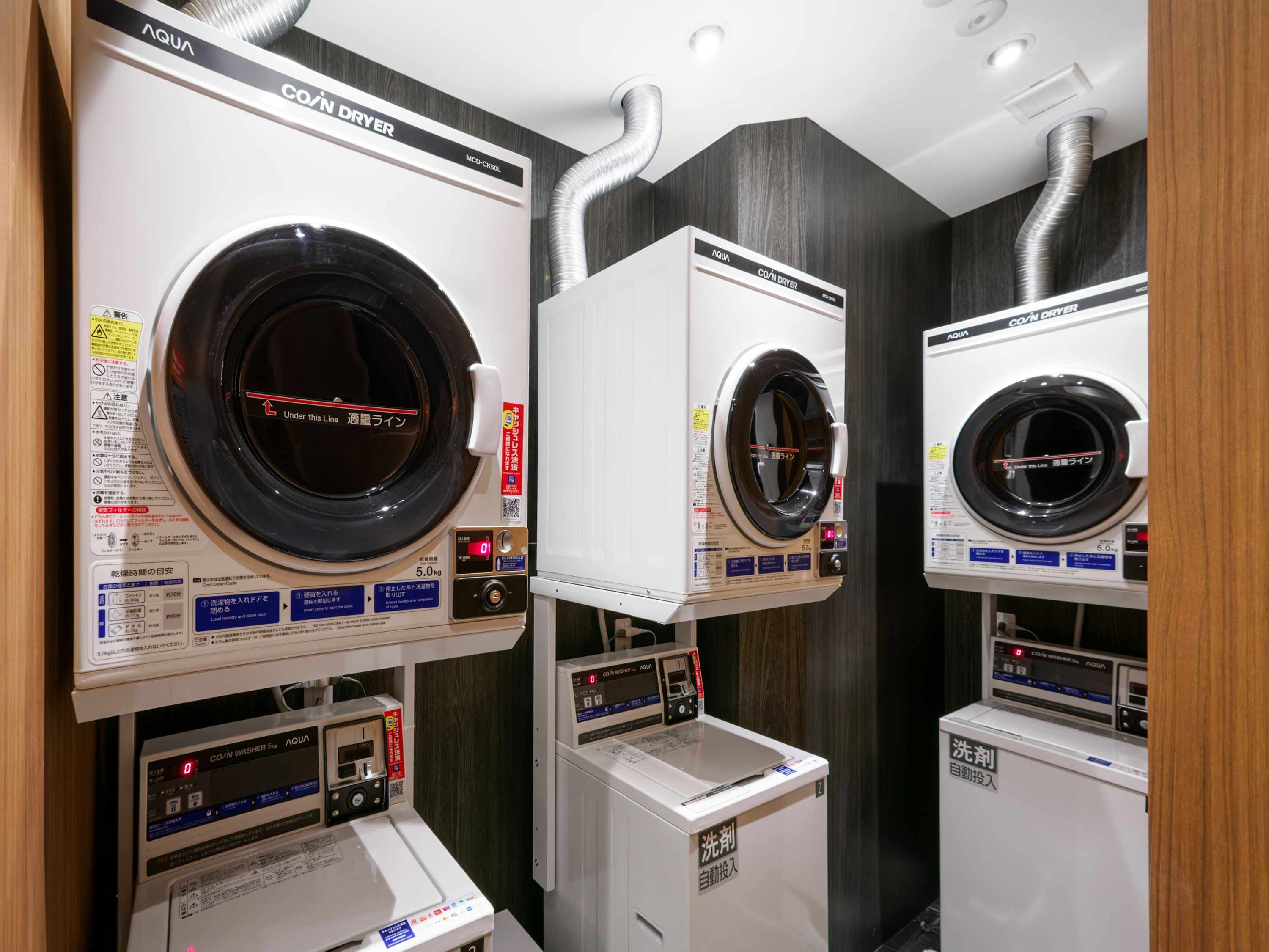 A row of coin-operated dryers with control panels and a washing machine below.