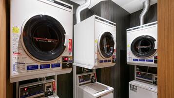A row of coin-operated dryers with control panels and a washing machine below.