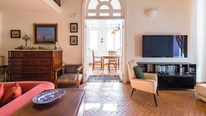 A living room with a herringbone floor, a television, a bookshelf, and a dining area with a table and chairs. - Residenza Capano Charming House by Napoliapartments (Naples)