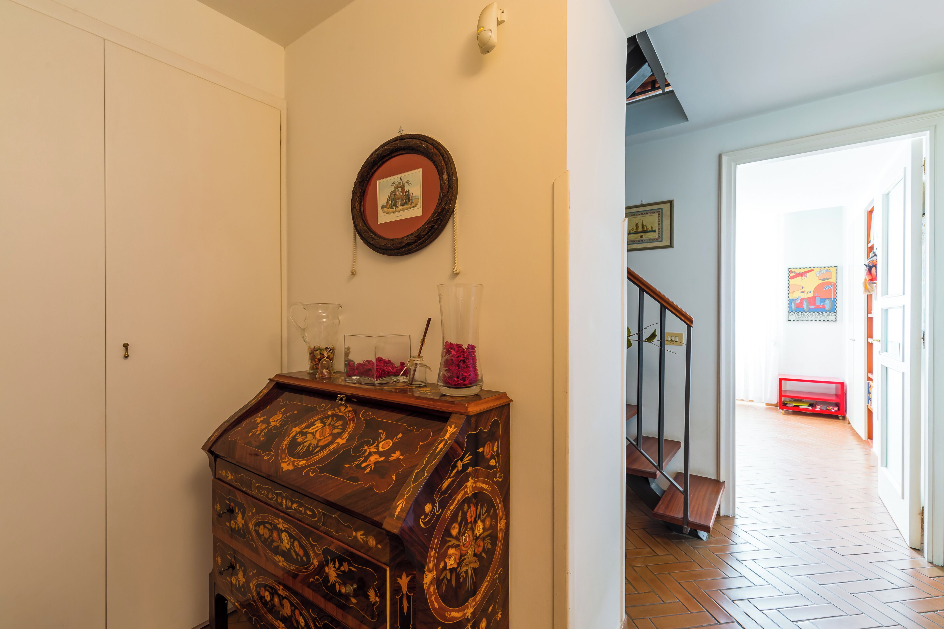 A wooden dresser with drawers, a framed picture on the wall, and a staircase leading to another room.