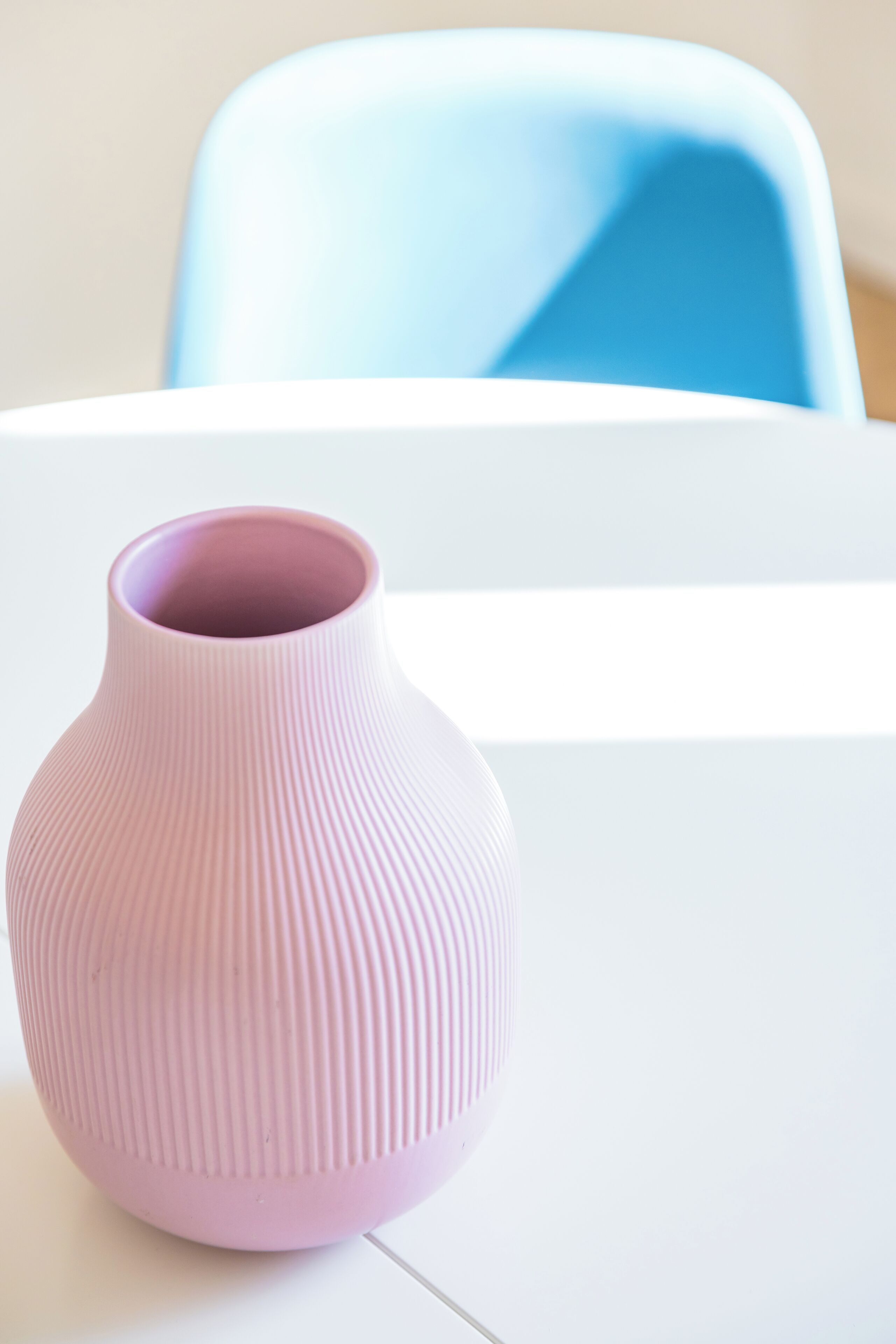 A pink vase on a white table with a blue chair in the background.