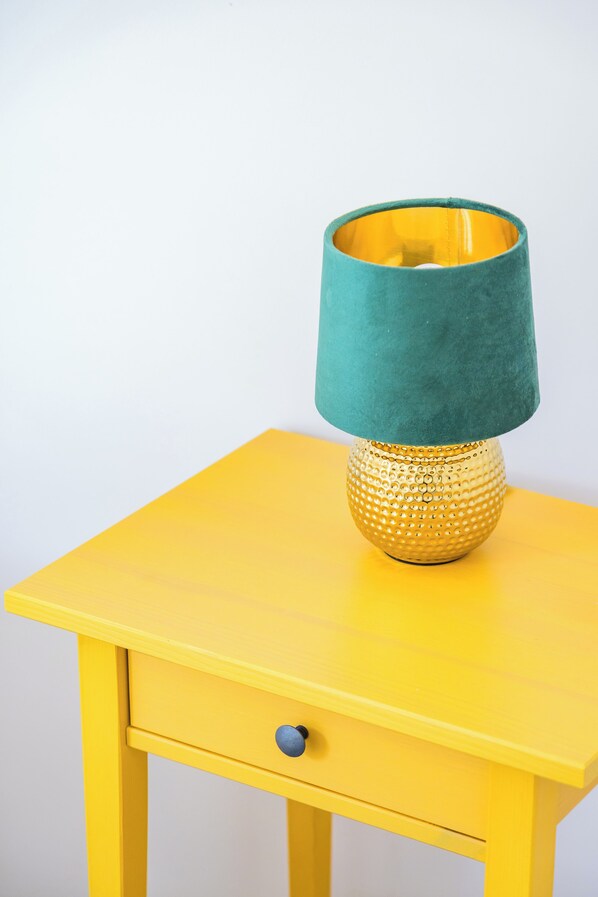 A yellow bedside table with a drawer and a lamp with a green lampshade. - Sunny Panoramic Apartment by Napoliapartments (Naples)