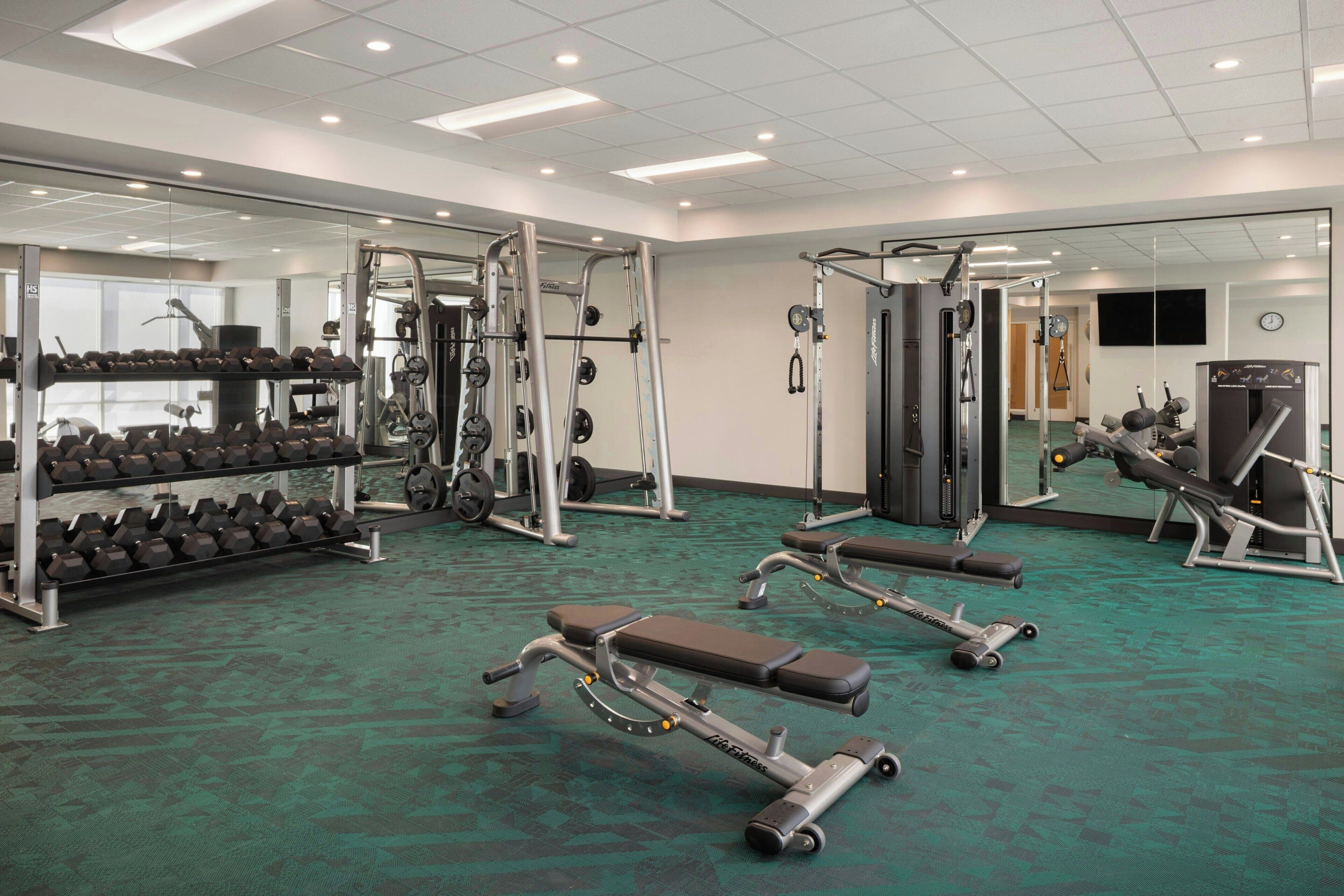 Un gimnasio con equipo de levantamiento de pesas, bancos y mancuernas.