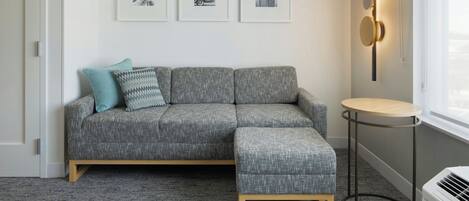 A modern living room with a grey sectional sofa, a small round table, and a wall-mounted light fixture.