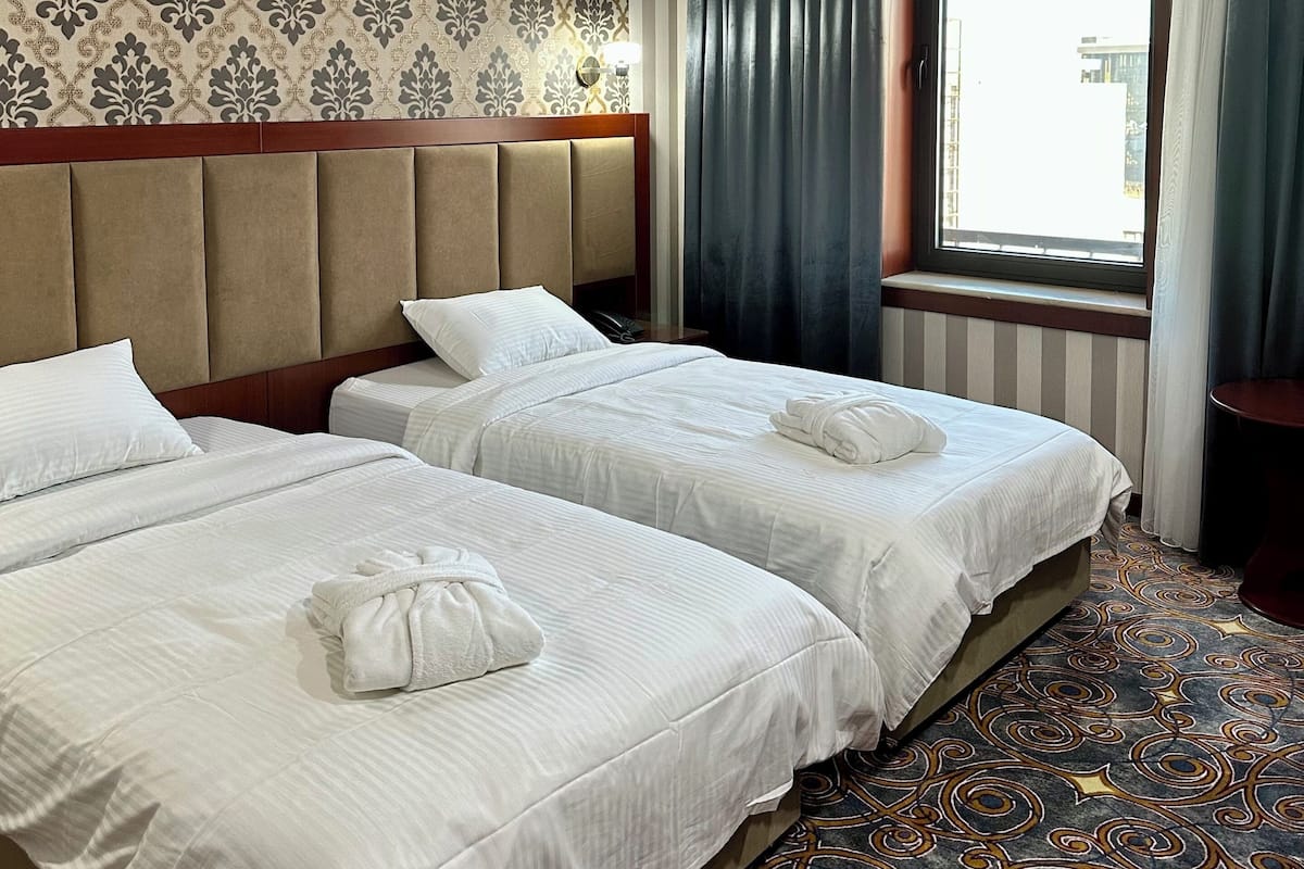 A hotel room with two beds, striped curtains, a patterned carpet, and a window with a view.