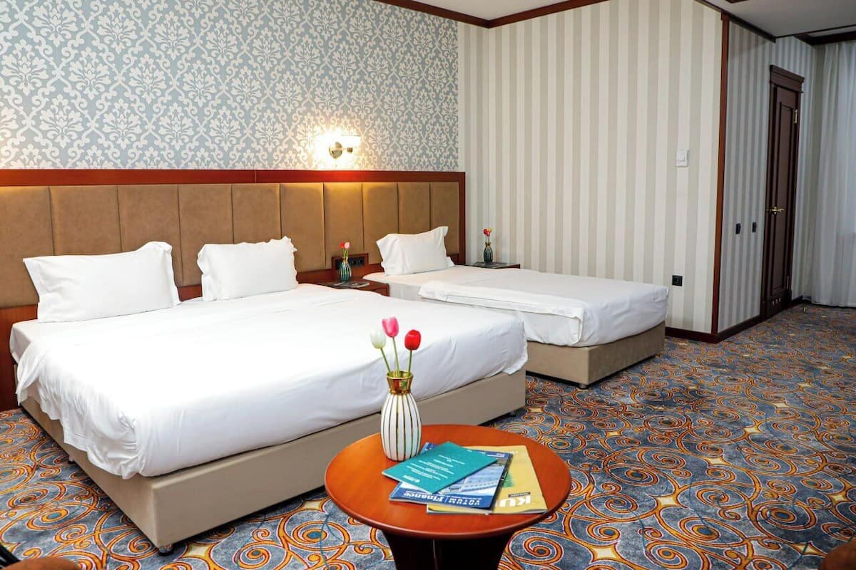 A hotel room with two beds, a nightstand, a vase with flowers, and a round table with books.